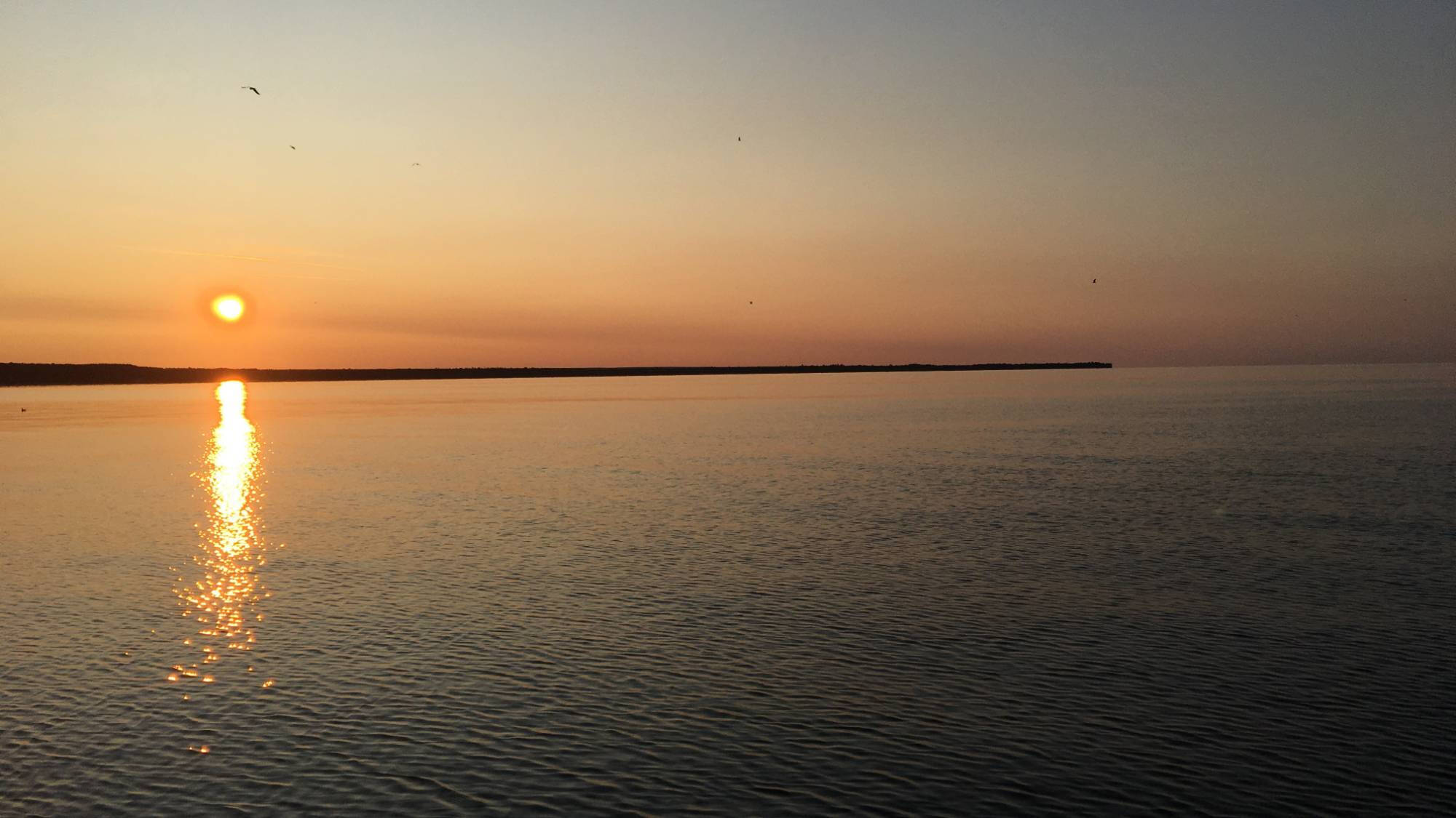 A setting sun sets the sky orange over a lake.